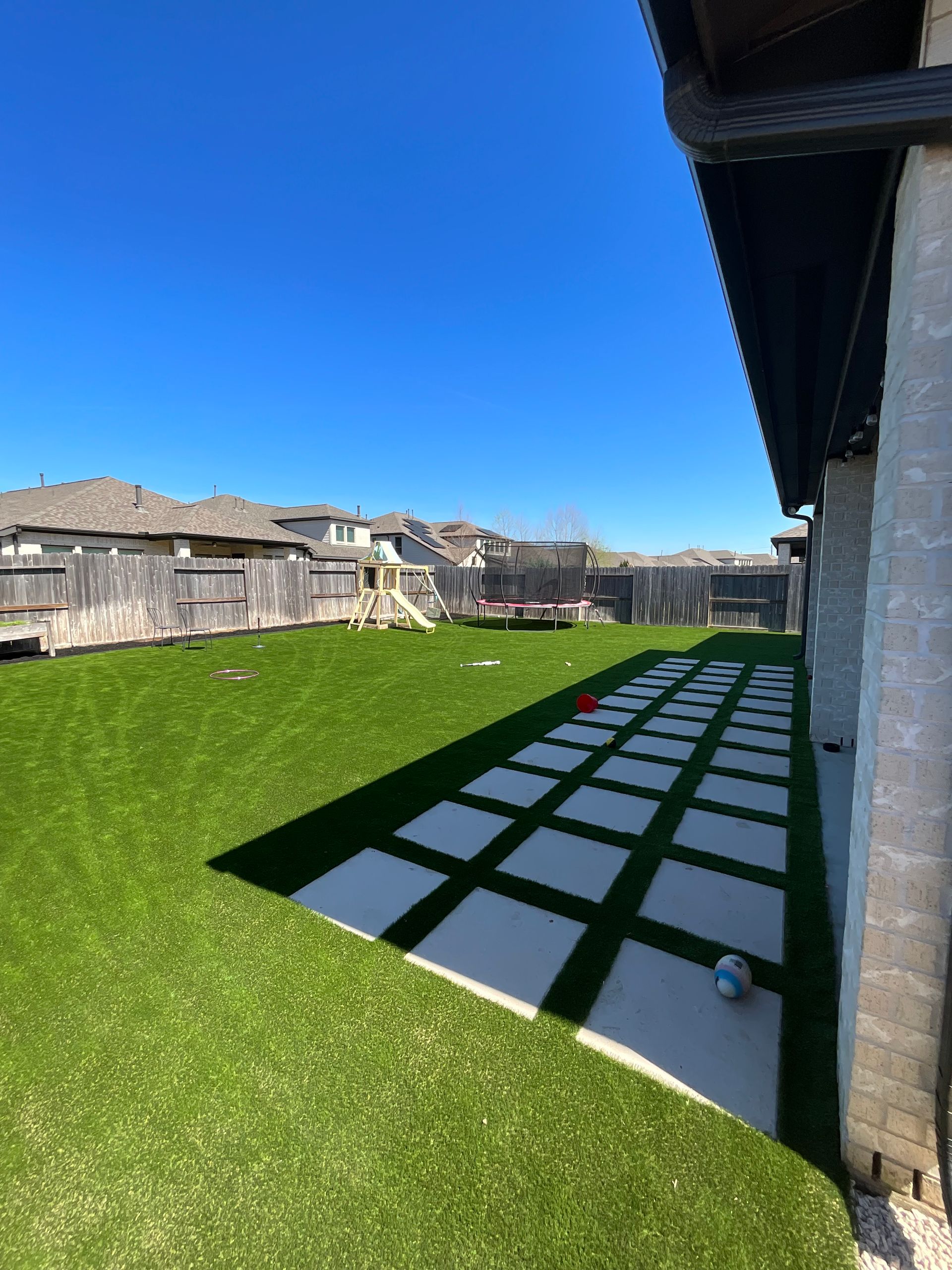 Backyard with green lawn, stone patio squares, and a clear blue sky