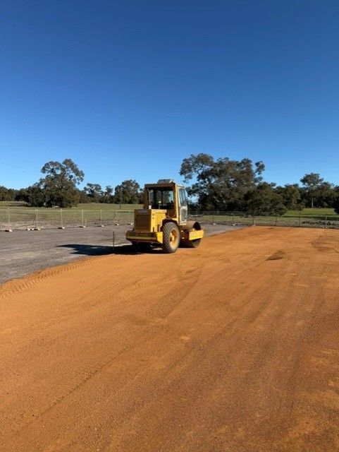 Yellow construction loader smoothing an orange dirt road under a clear blue sky