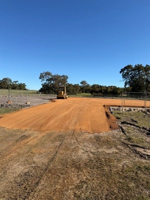 Freshly graded orange dirt road with a construction roller under a clear blue sky