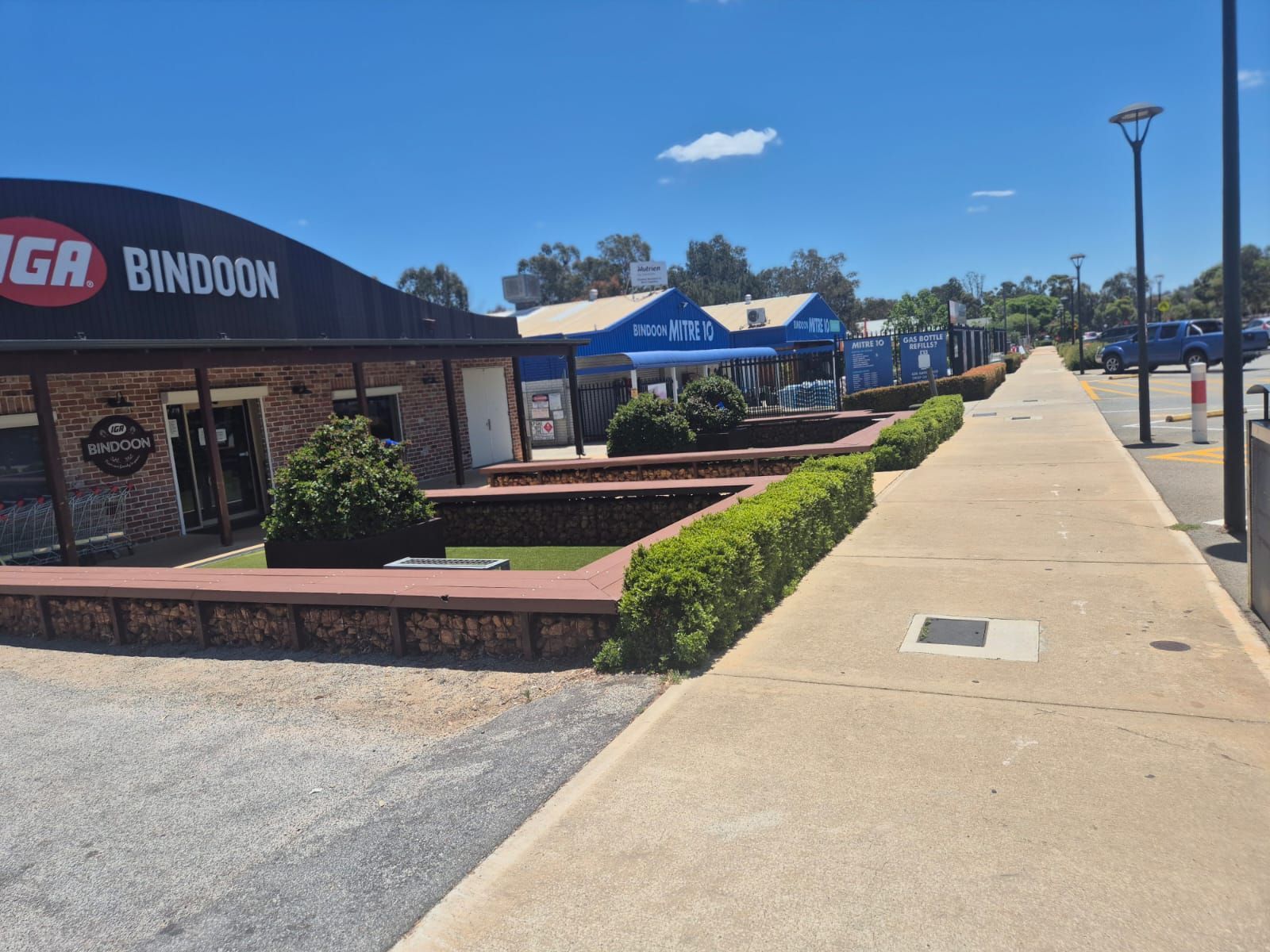 Shopping center walkway beside a BINGO BINDOON storefront, with brick planters and blue shade tents.