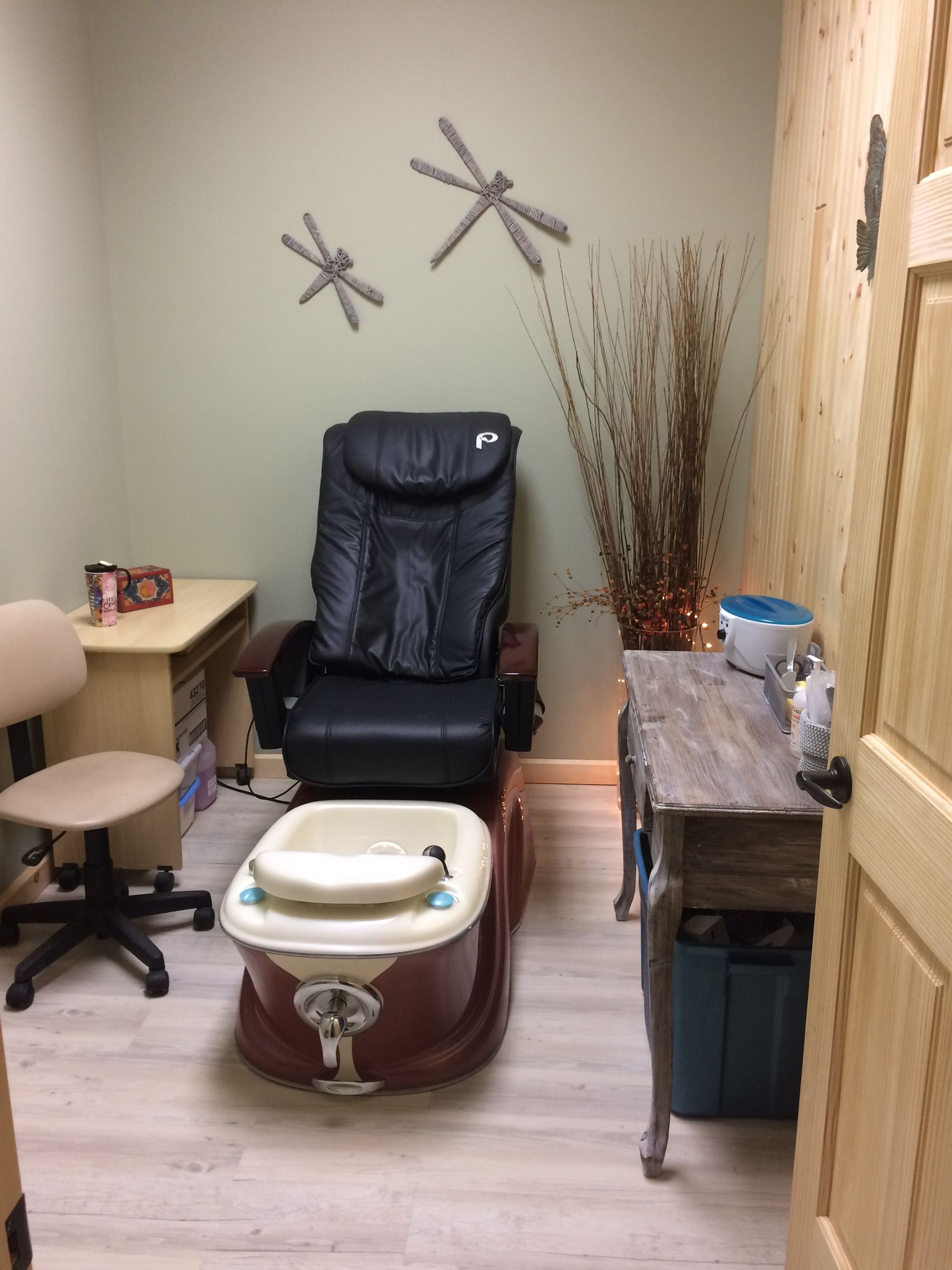 A pedicure chair with a foot bath sits in a room with light-colored flooring, a small desk, and a decorative console table.