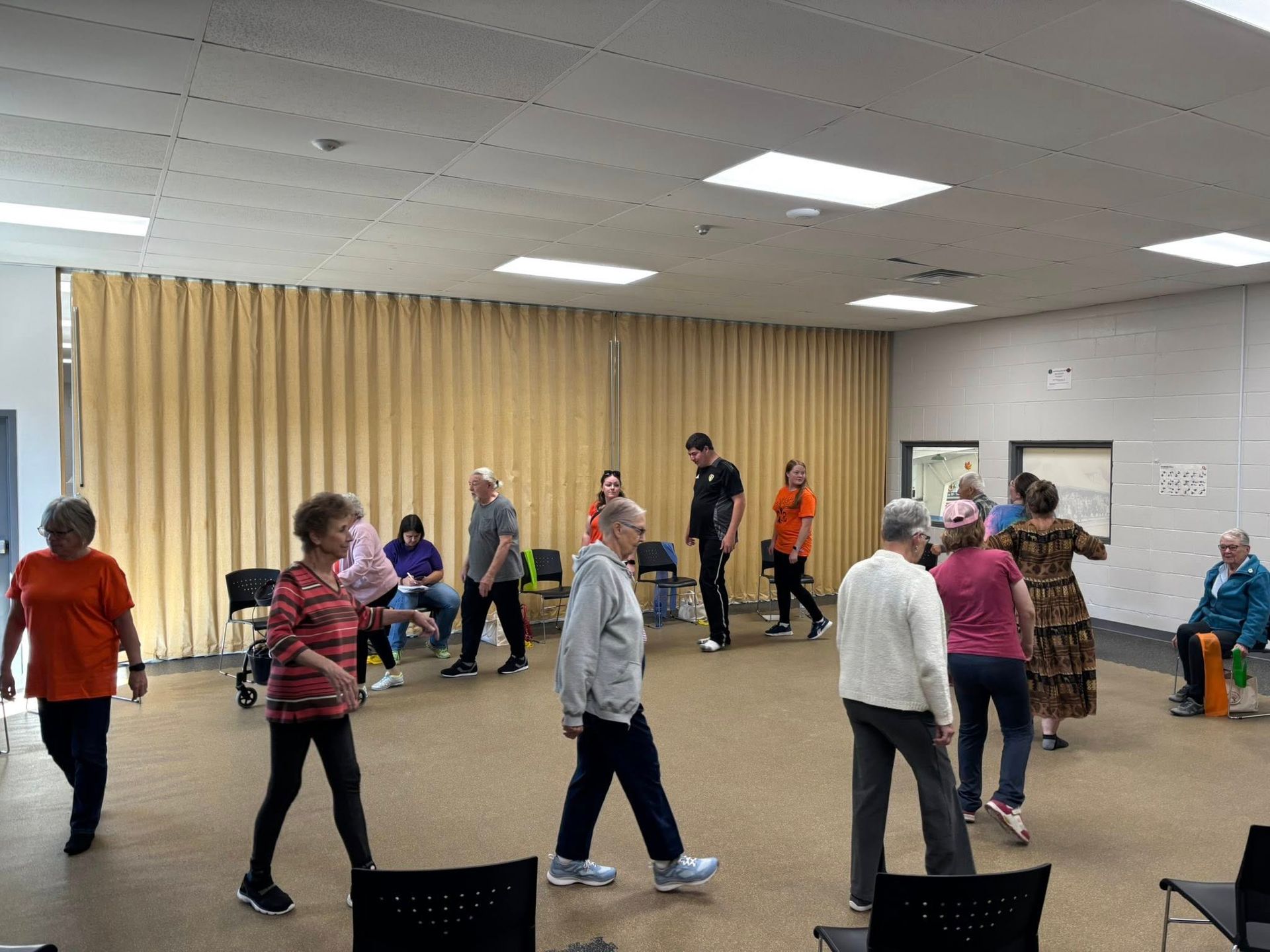 A group of people in an indoor hall practicing gentle movement exercises, moving together in a spacious room.