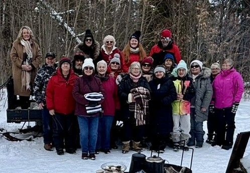A large group posing together outdoors in a snowy, wooded area, wearing winter clothing and warm hats.