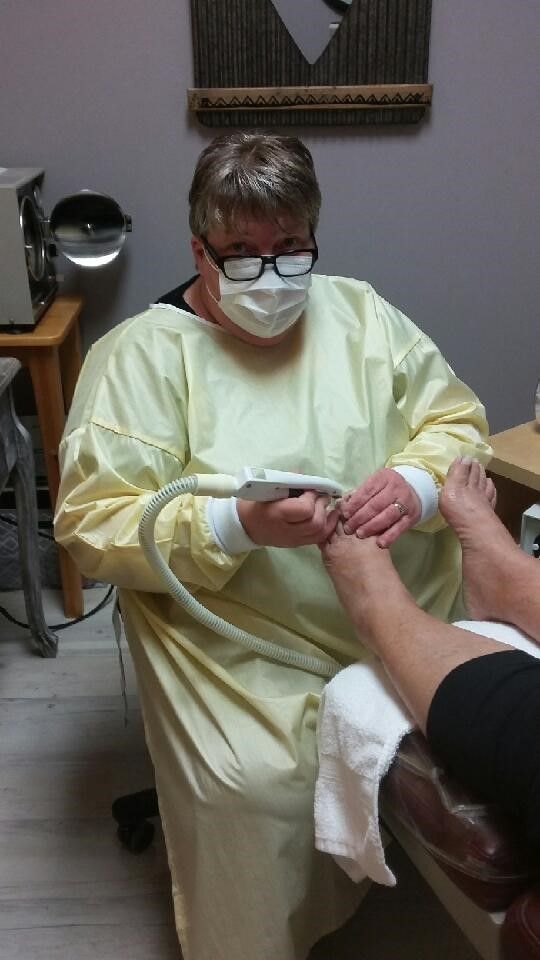 A healthcare provider wearing a yellow gown and mask uses a handheld device to treat a patient's foot in a clinic.