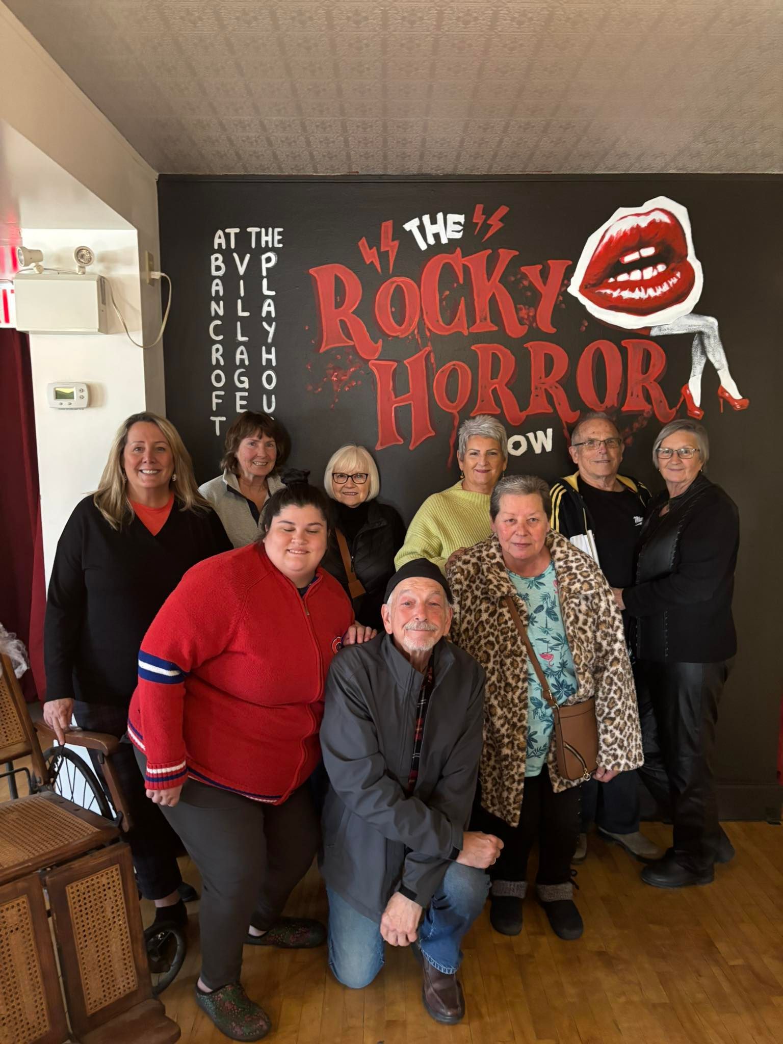 A group of nine people smiling in front of a painted 