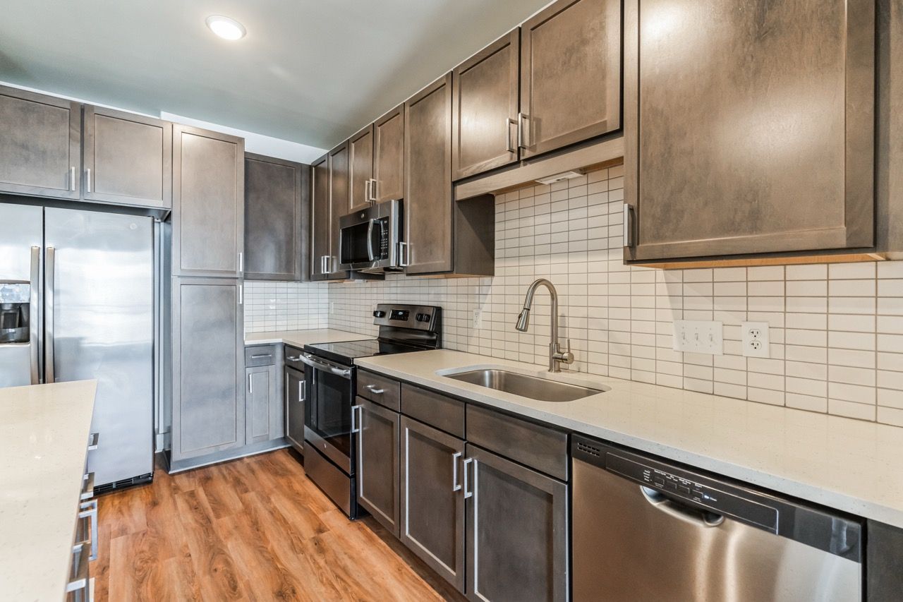 Modern kitchen with stainless steel appliances, gray cabinets, and a white tile backsplash.