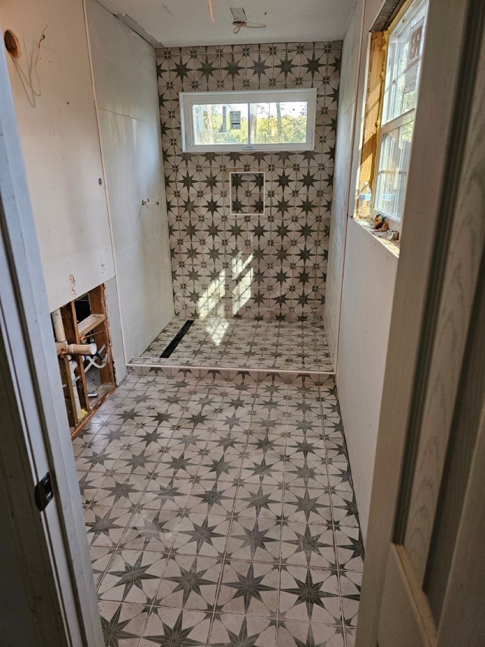 Narrow tiled hallway with star-pattern floor and wall tiles, a window at the far end, and a doorway on the right