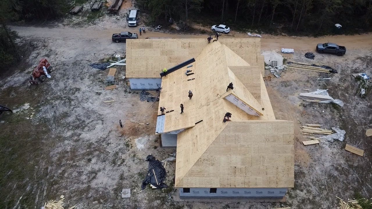 Aerial view of a house under construction with a new roof and scattered materials on a dirt lot.