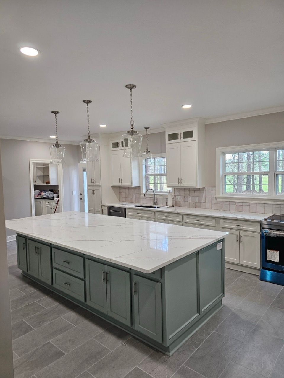 Modern kitchen with large island, white countertops, green cabinets, and pendant lights