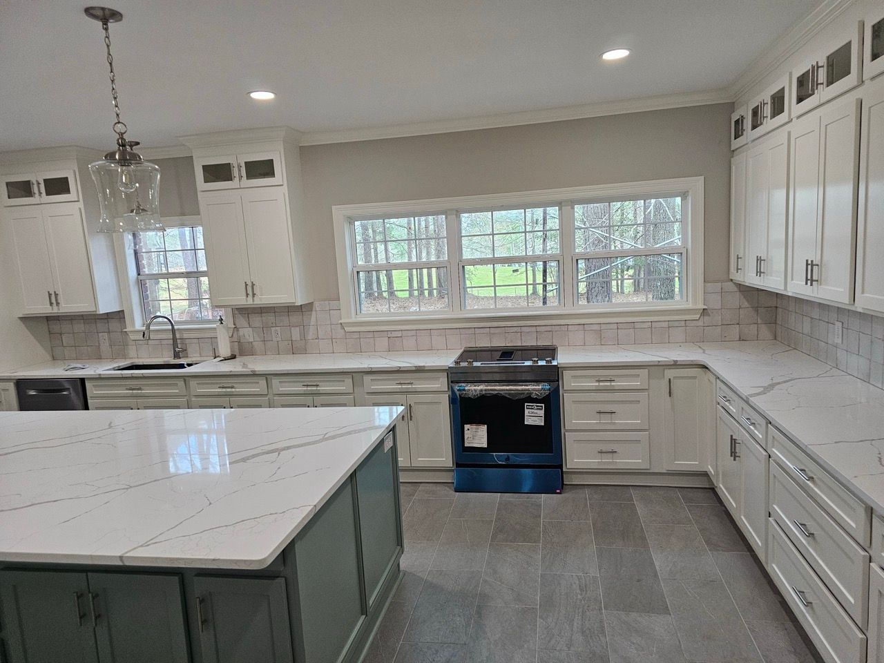 Bright modern kitchen with white cabinets, marble island, and a large window over the sink.