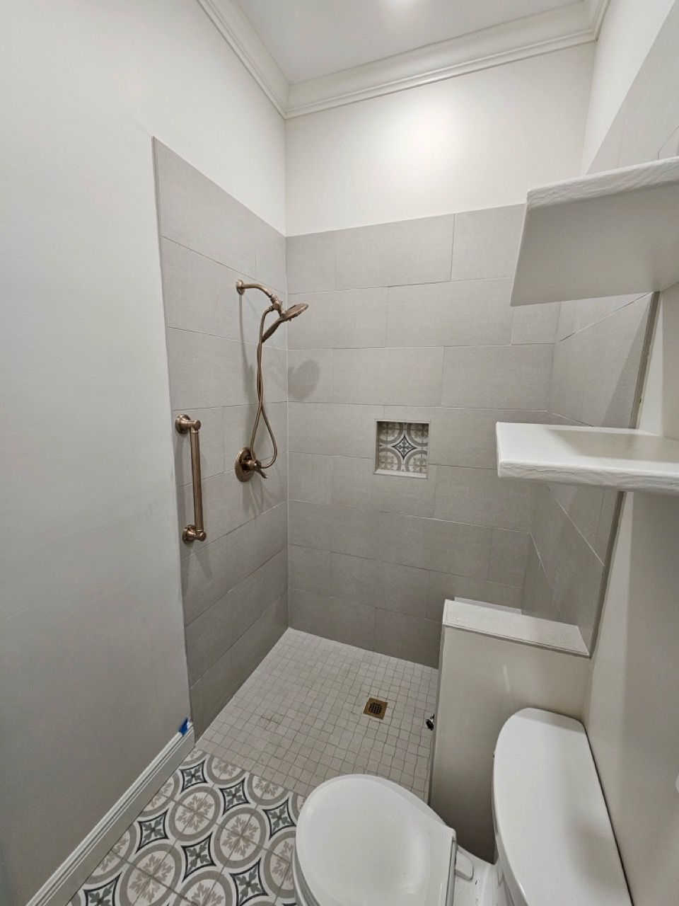 Small tiled shower and toilet in a compact bathroom with white walls and shelves