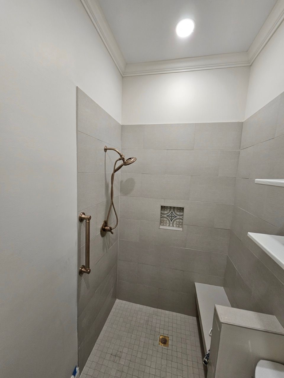 Empty tiled shower with bench, wall-mounted showerhead, and recessed light in a small bathroom