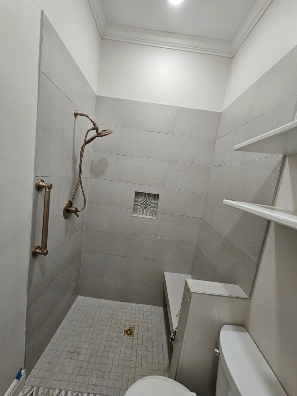 Small unfinished bathroom with tiled shower, exposed plumbing, toilet, and wall shelves