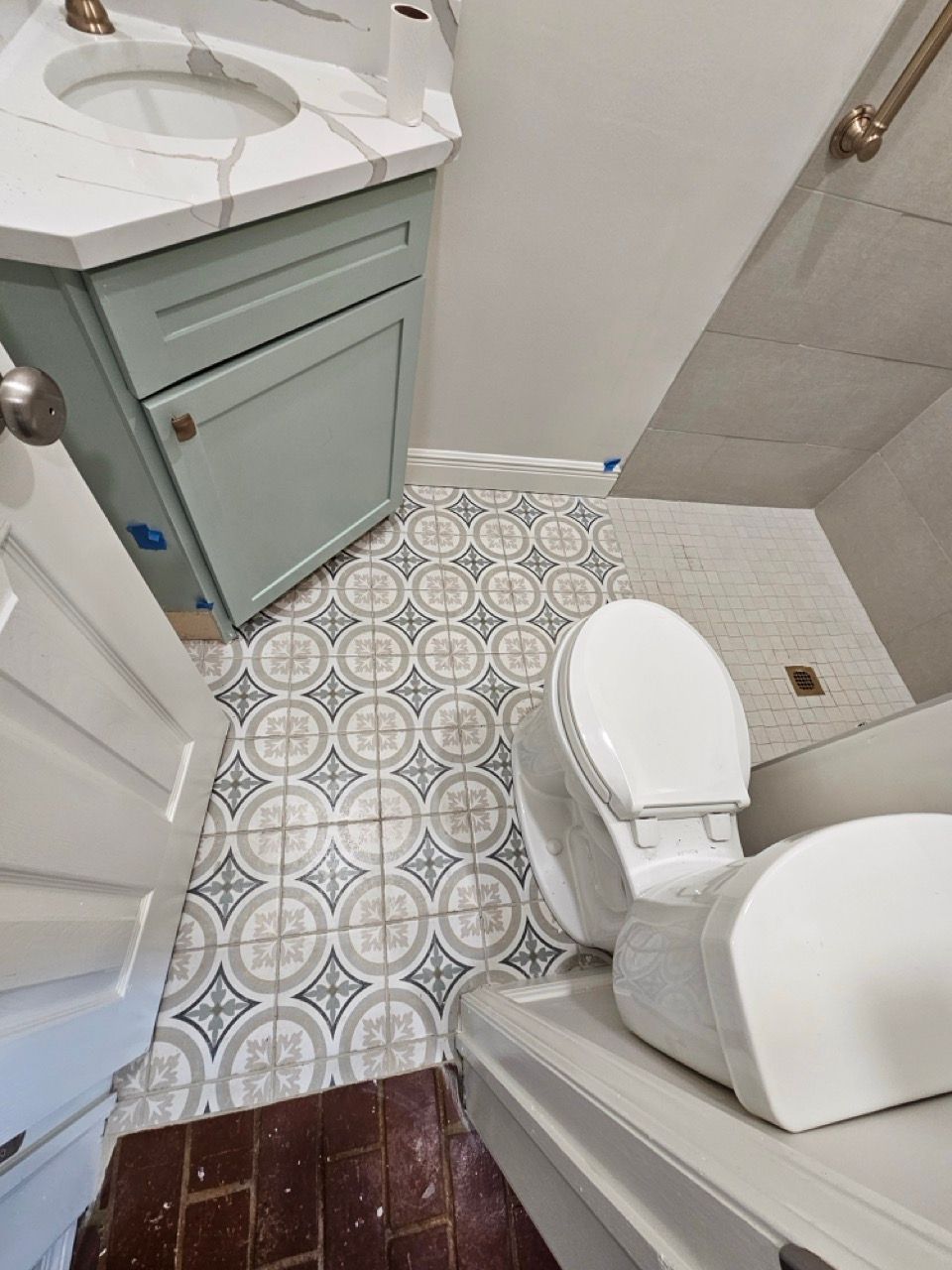 Small bathroom with patterned tile floor, white toilet, sink vanity, and shower door.