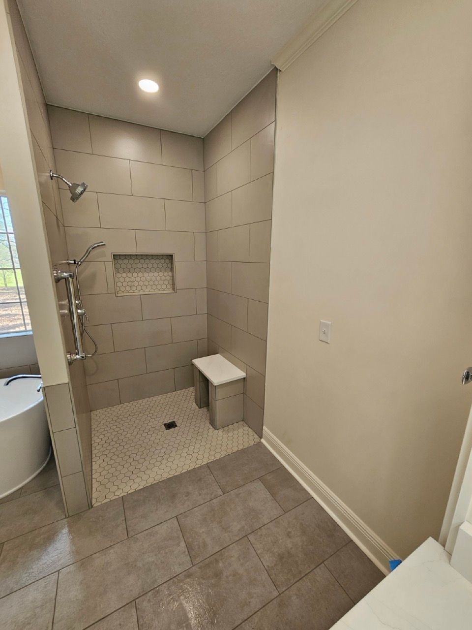 Small tiled shower with bench and recessed shelf, viewed from a bathroom doorway.