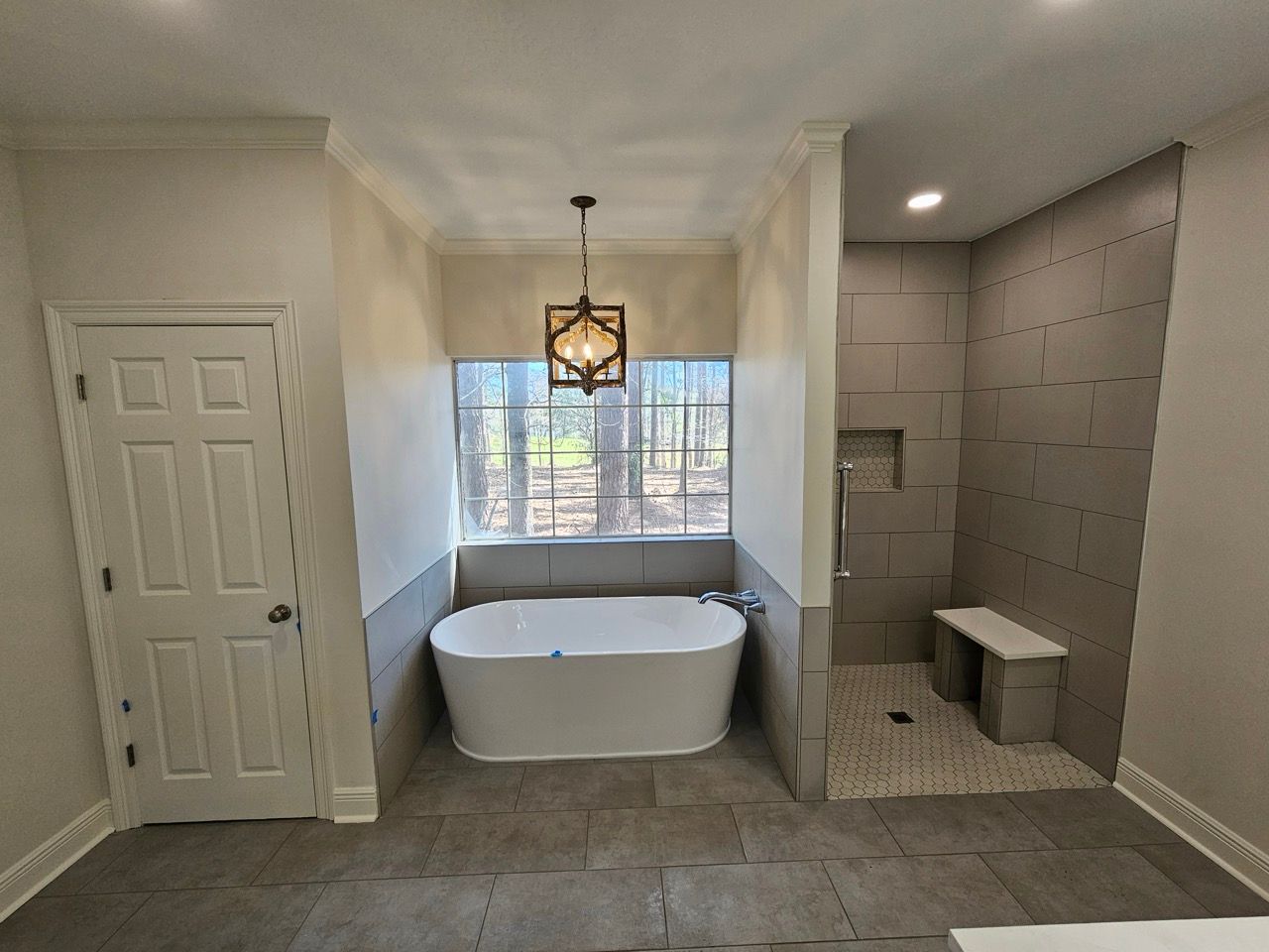 Bright bathroom with freestanding tub under a window, tiled shower wall, and closed white closet doors
