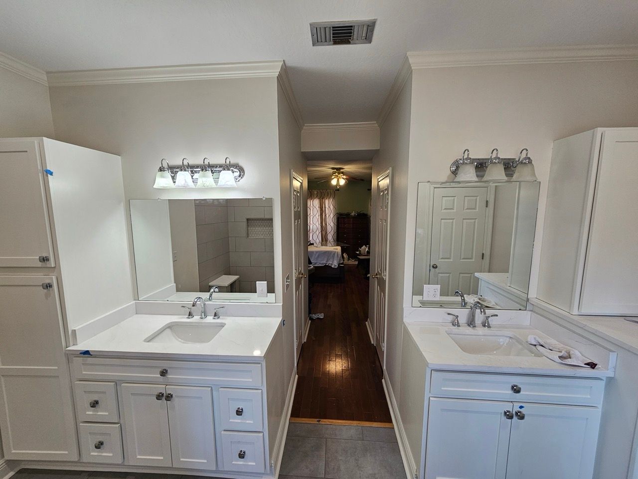Bathroom with double sinks, mirrors, vanity lights, and a hallway leading to a darker room.