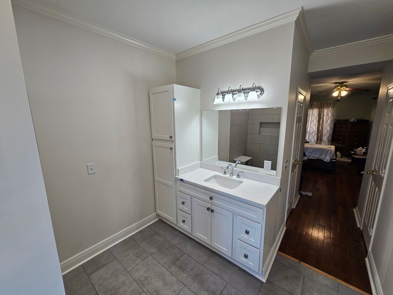 Small kitchen with white cabinets, sink, mirror, and tiled floor leading to a dark hallway.