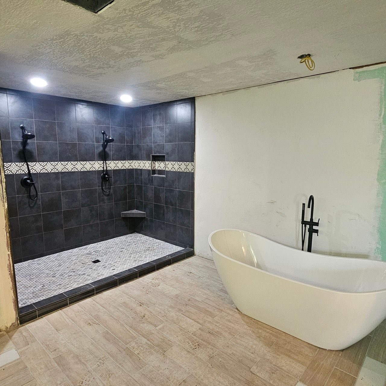Modern bathroom with black tile walk-in shower and freestanding white tub on light wood floor