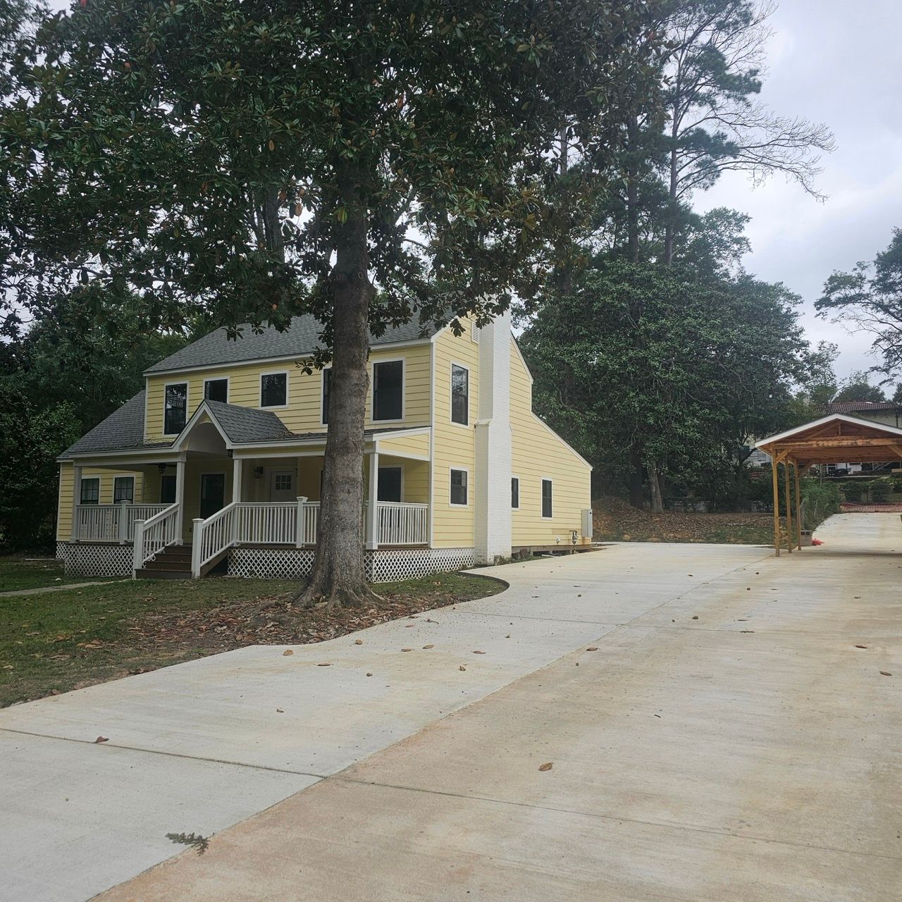 Two-story yellow house with a large driveway, surrounded by trees and a small porch.