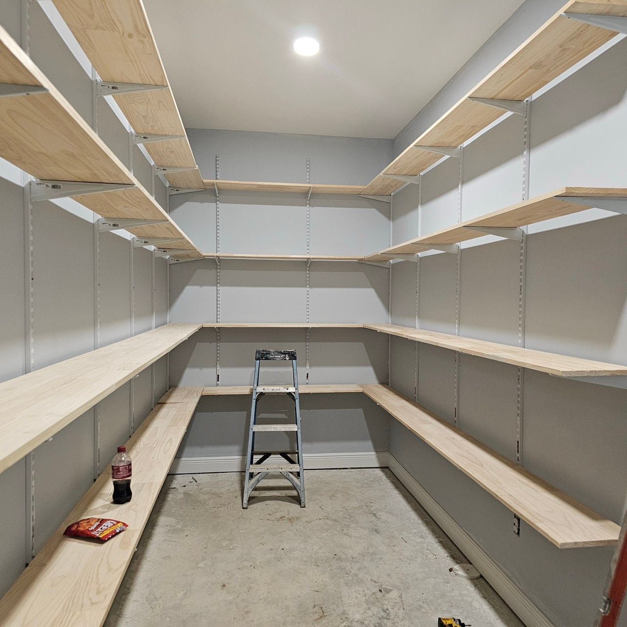 Empty walk-in closet with white shelves, beige walls, and a stepladder in the center