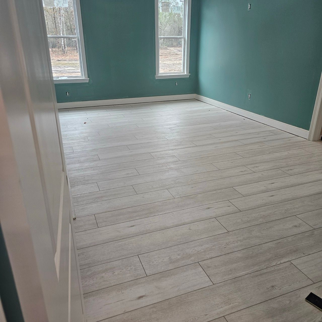 Empty teal room with white wood floors and two windows looking outside