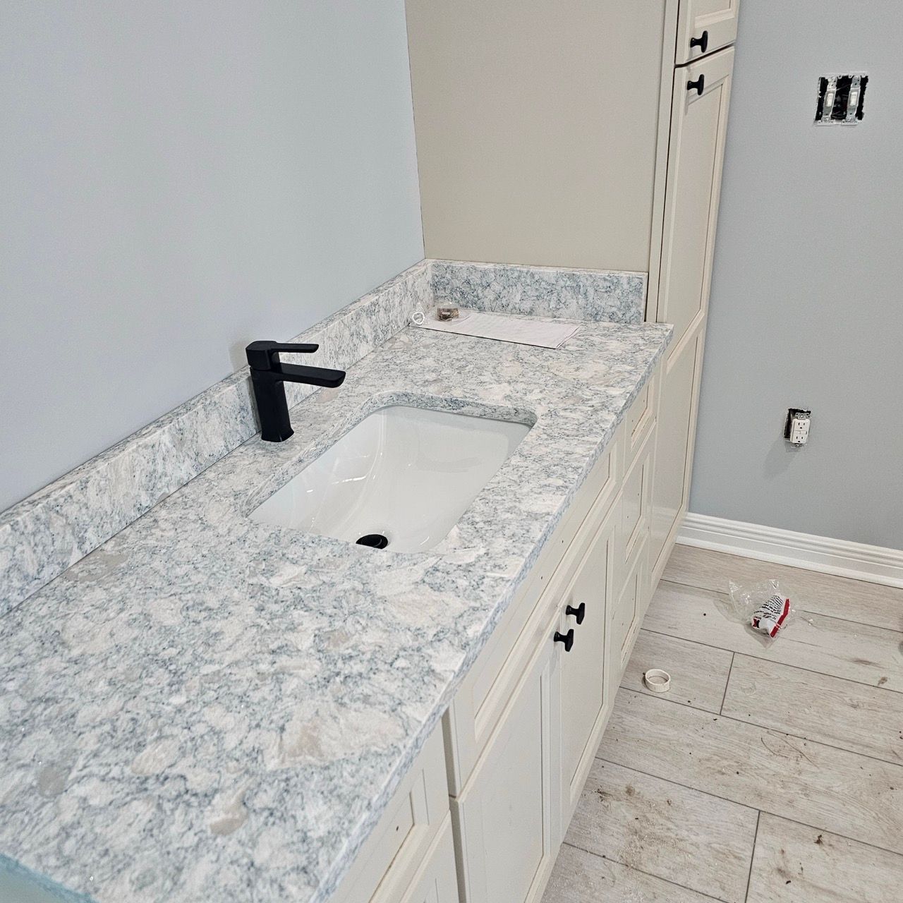 Modern bathroom vanity with white-and-gray countertop, black faucet, and sink under construction