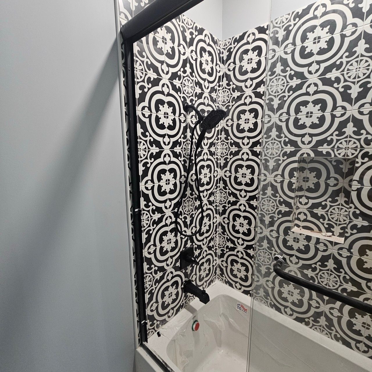 Black-and-white patterned shower stall with a glass door and tub faucet.
