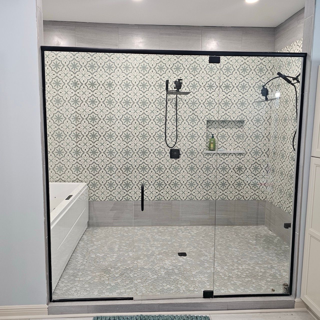 Modern bathroom shower with patterned tile, glass enclosure, and white vanity sink