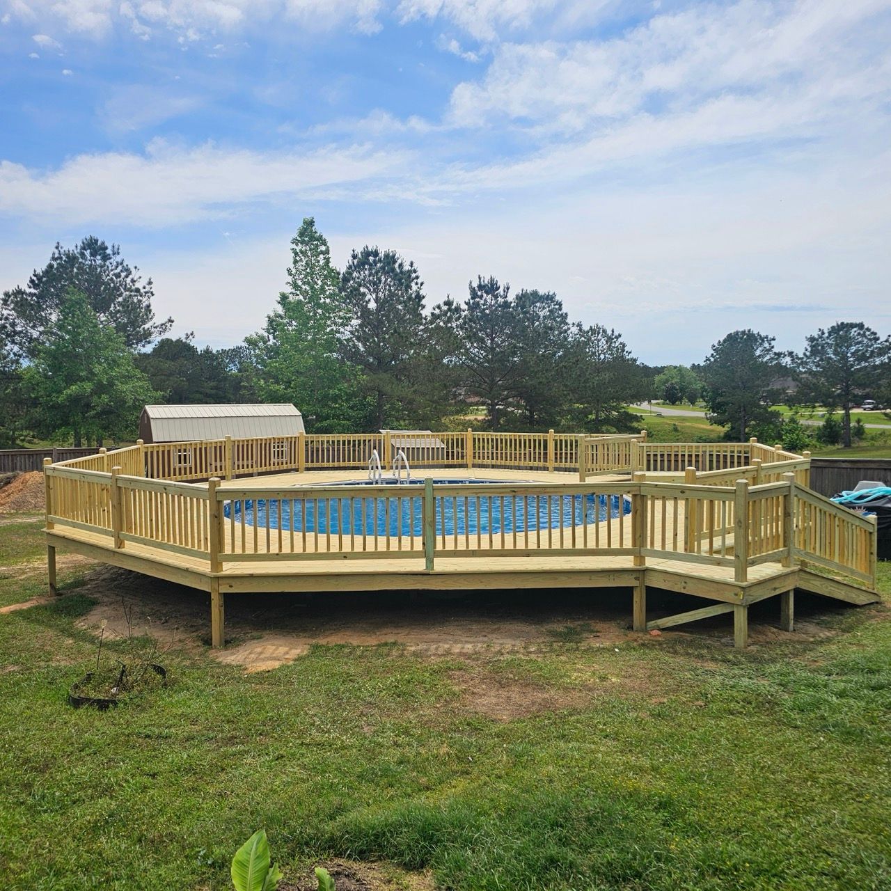 Round above-ground pool with wooden deck railing in a grassy yard under a cloudy sky