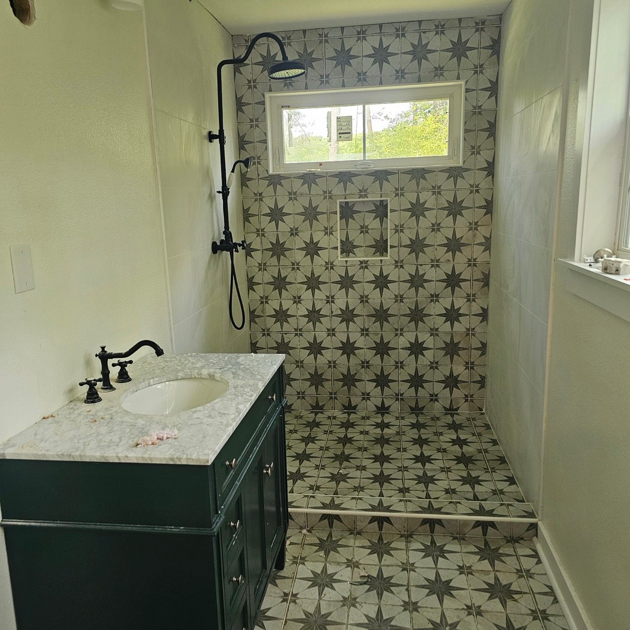 Small bathroom with patterned shower, white sink vanity, and a window above the shower.