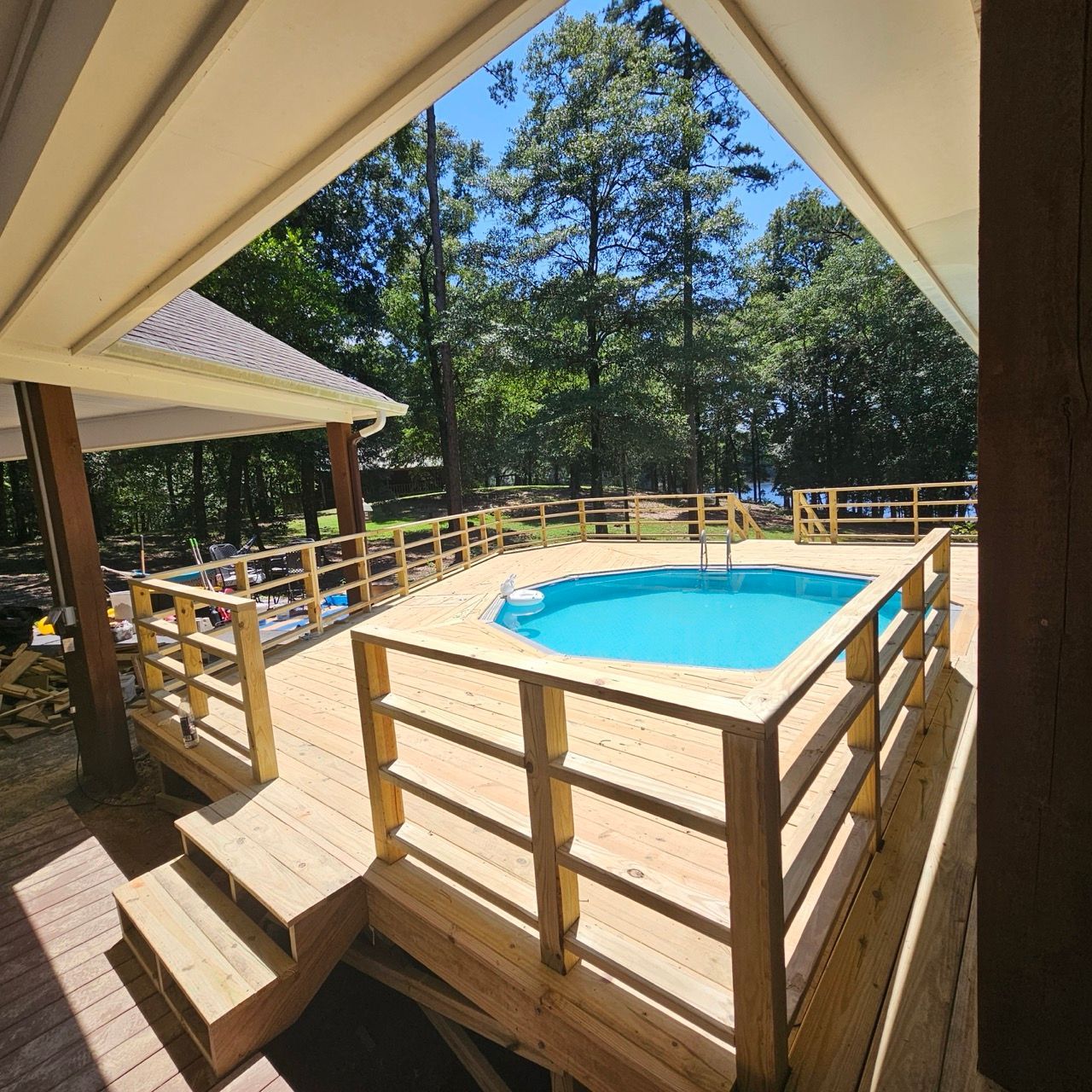 Covered deck overlooking a small blue swimming pool surrounded by wooden railings and trees