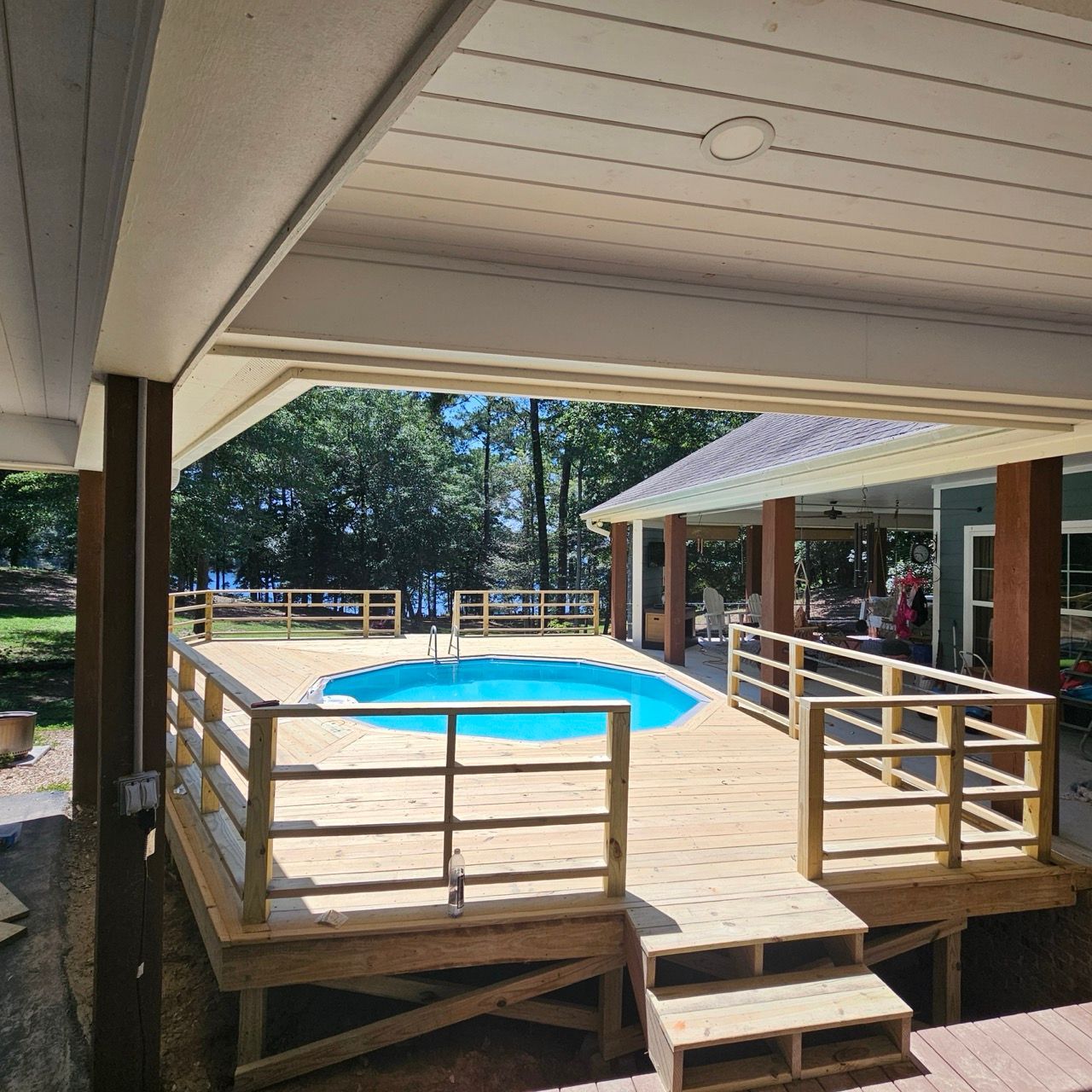 Covered patio overlooking a small blue pool with wooden railings and steps in a sunny courtyard