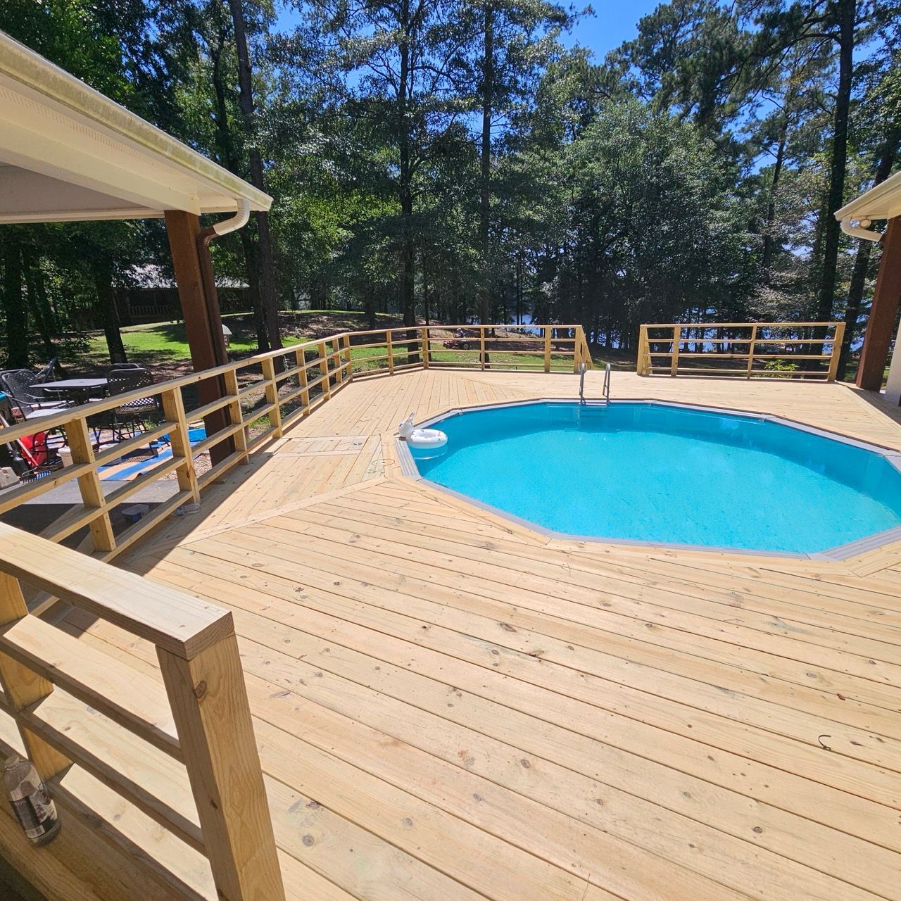 Wooden deck surrounding a small blue pool in a wooded backyard, with railings and covered seating areas.