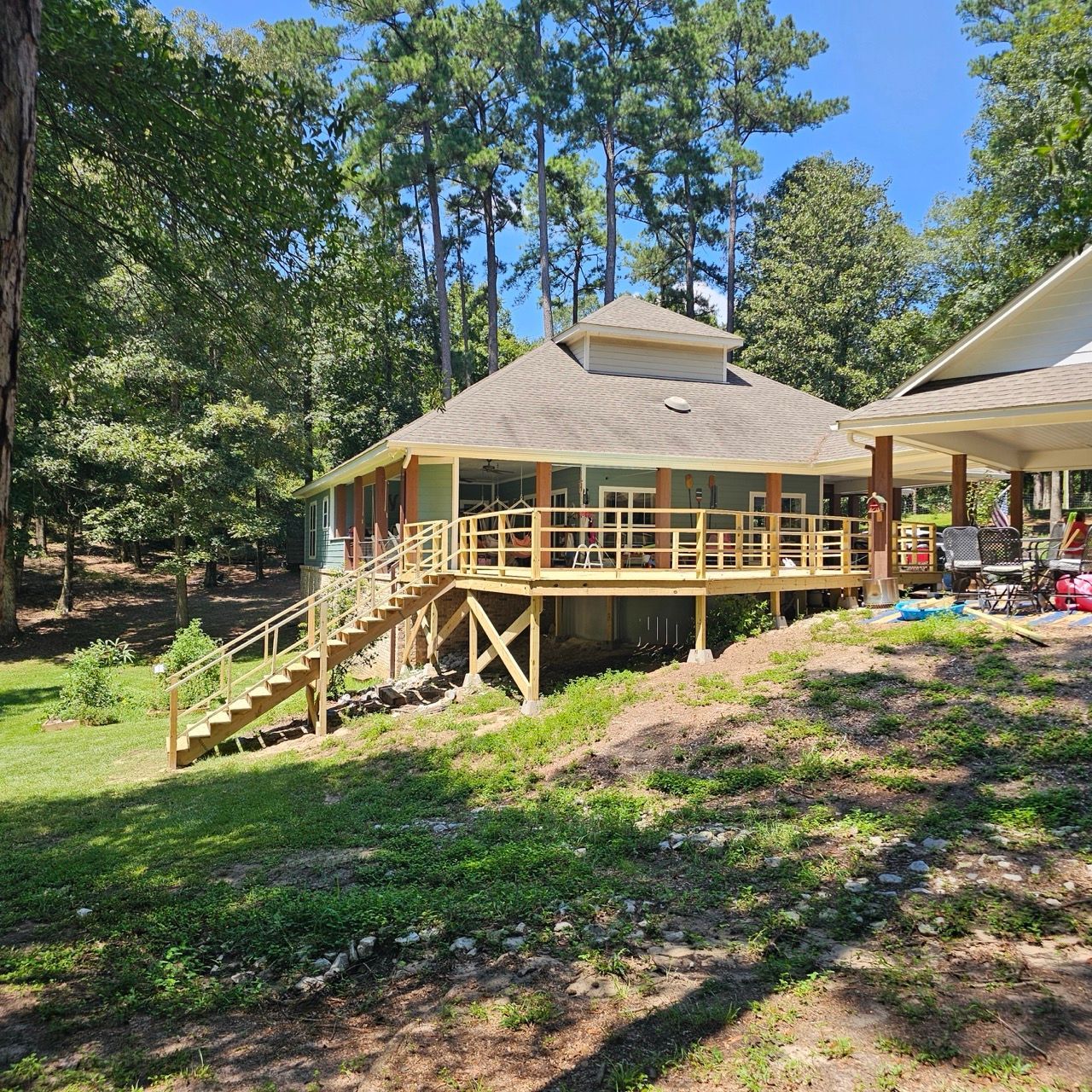 Wooden cabin with porch and stairs in a wooded yard under a blue sky