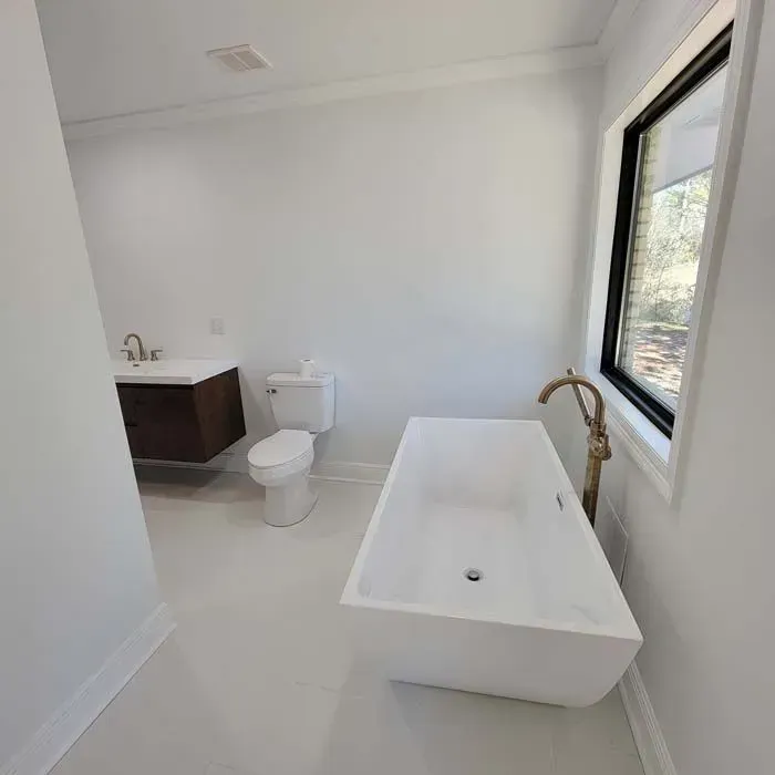 Modern white bathroom with a freestanding tub, toilet, and vanity, near a window.