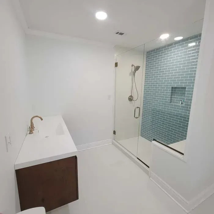 Bathroom with white walls and floor, a glass shower with blue tile, and a floating sink with brass faucet.