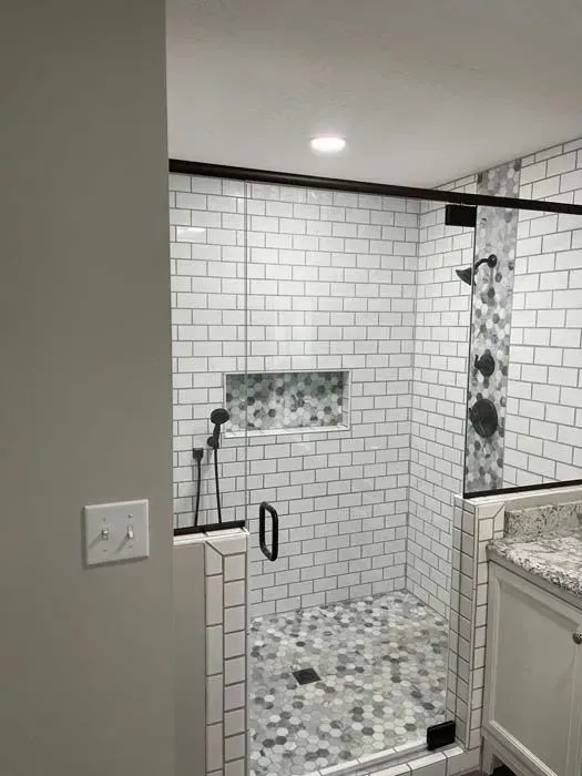 Modern bathroom with a glass-enclosed shower, white subway tile, and a gray and white hexagon tile floor.