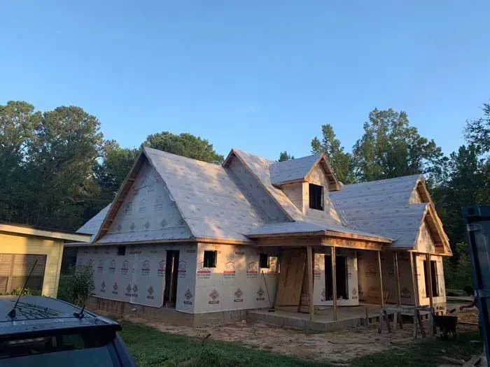 House under construction with wooden frame, unfinished roof, and wrapped walls in an outdoor setting.