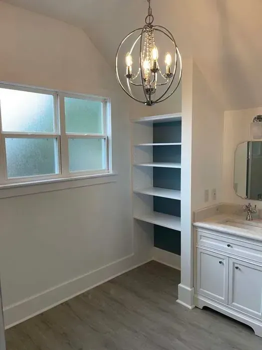 Bathroom with built-in shelves, vanity, frosted window, chandelier, white walls, and gray flooring.