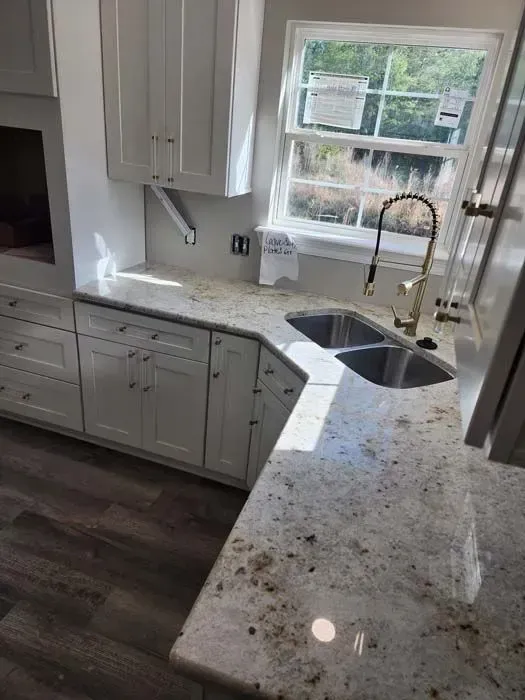 White kitchen with granite countertop and double sink near window.