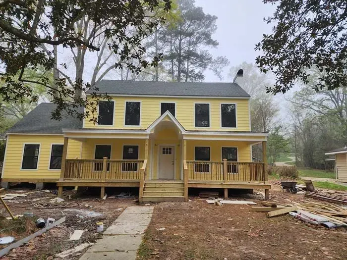 Yellow two-story house with porch, windows, and a dark roof on a cloudy day.