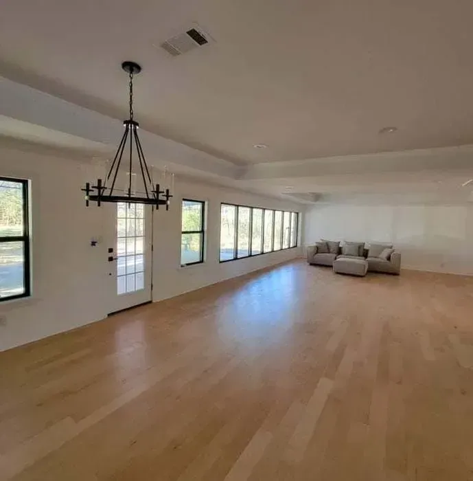 Spacious, light-filled room with wood floor, windows, a couch, and chandelier.