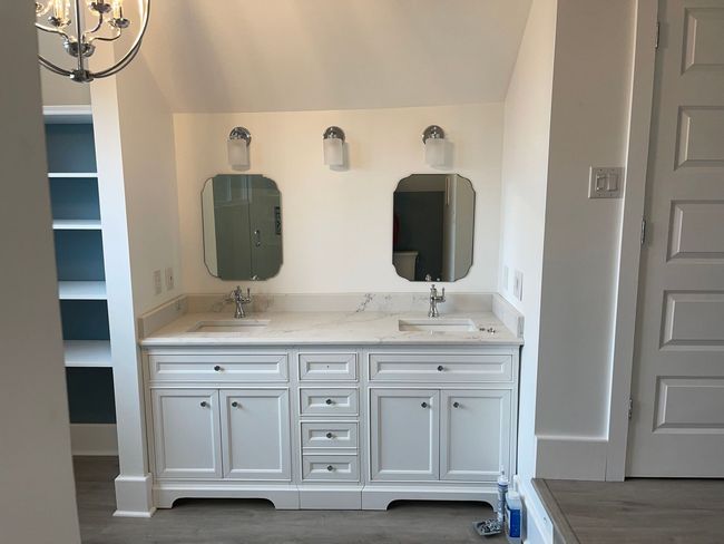 White bathroom vanity with two mirrors and sinks, lit by sconces, in an alcove.