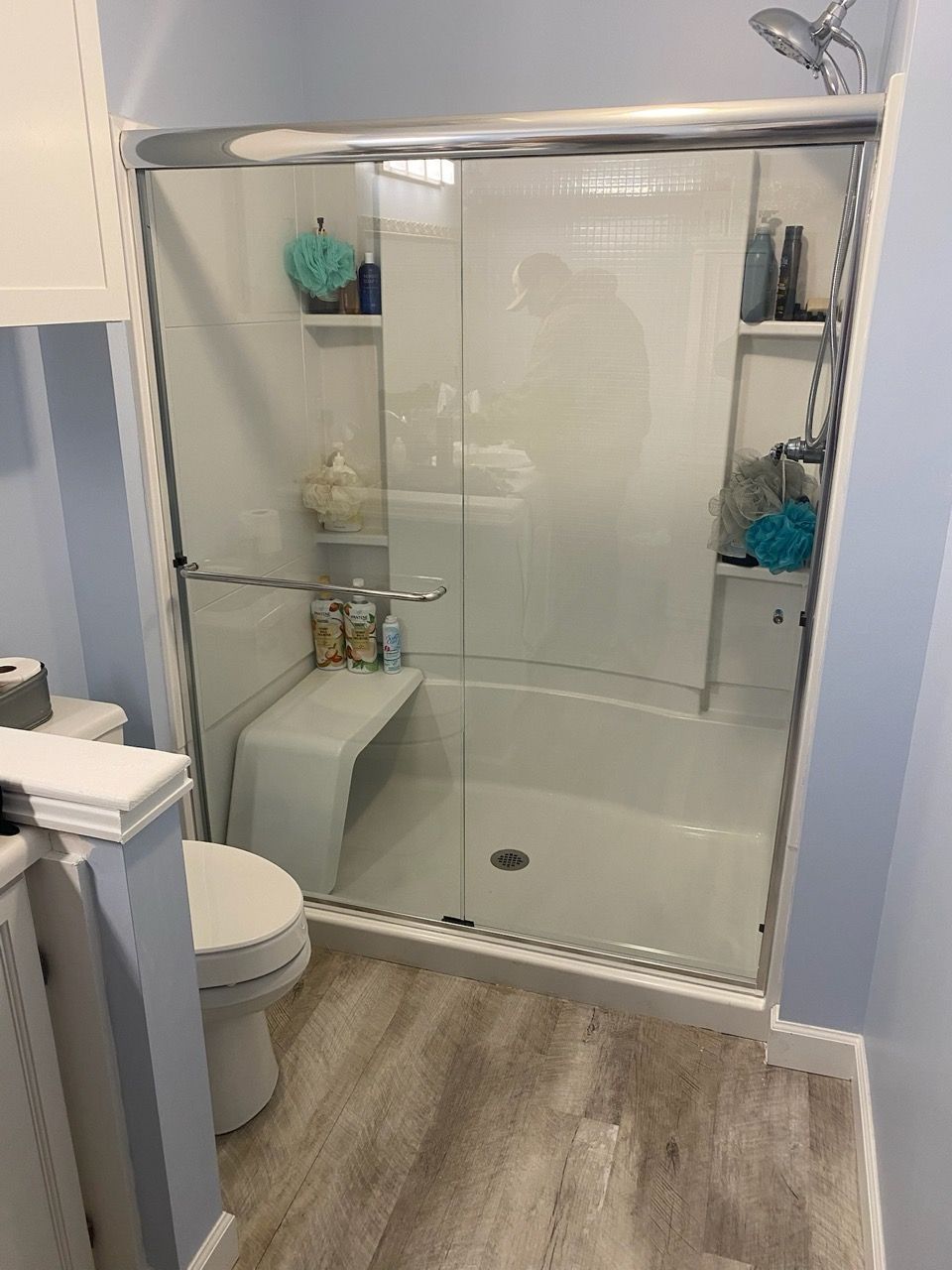Glass walk-in shower with chrome fixtures, white tile, corner shelves, and wood-look flooring in a bathroom