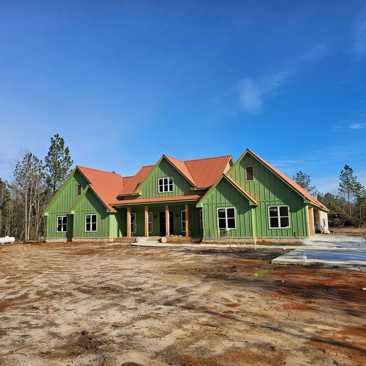 Green house with red roof on a bare lot under a clear blue sky