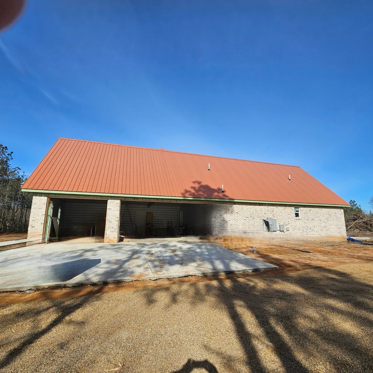 Stone house with a red metal roof and attached garage under a clear blue sky