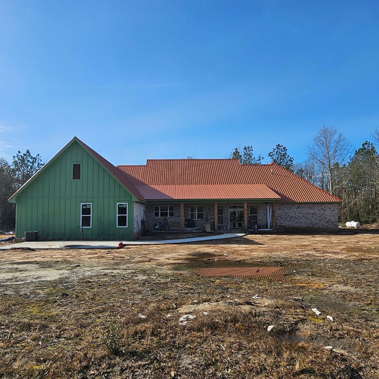 Green house with a red metal roof under construction on a bare lot under a blue sky