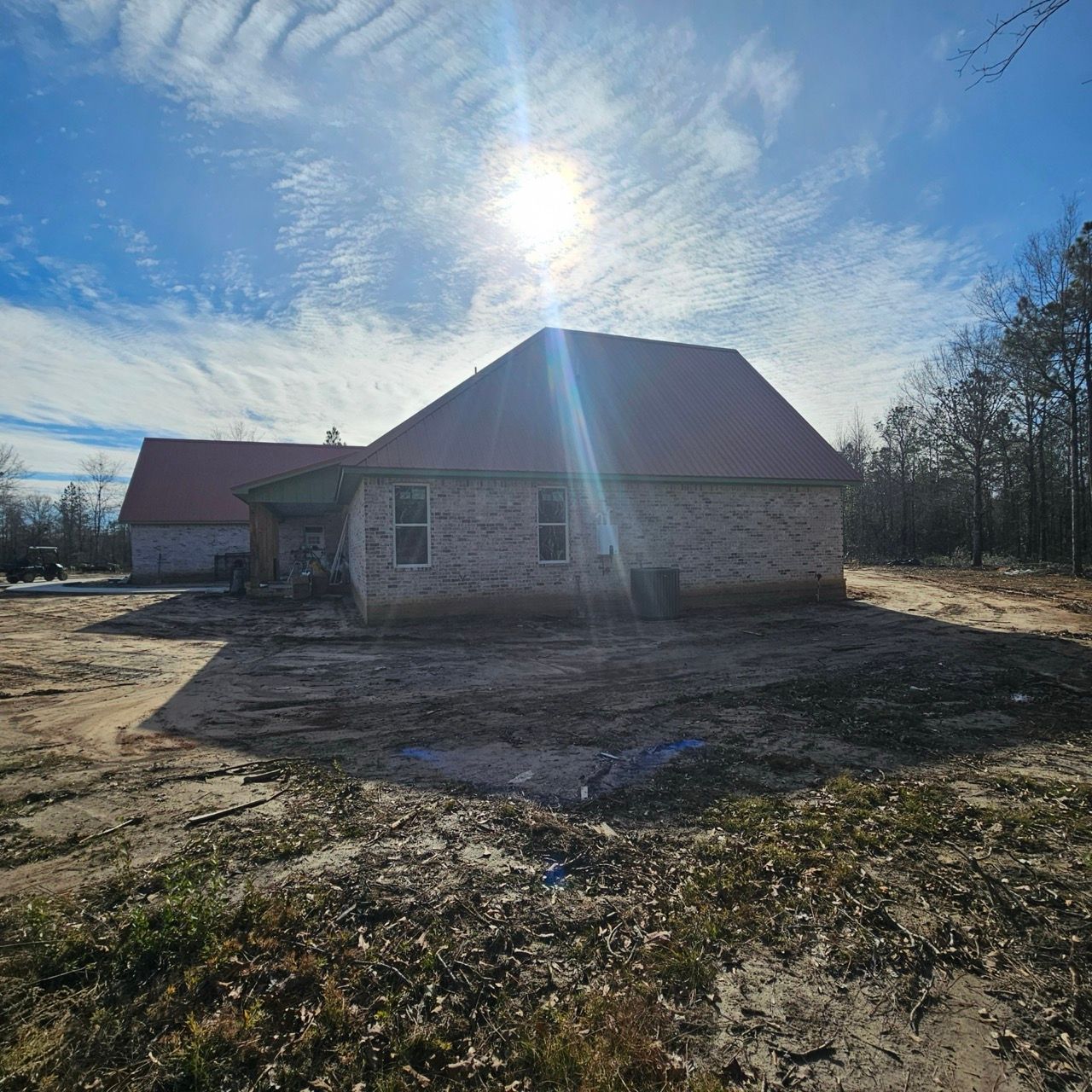 Stone house under construction in a sunny rural lot, with a red roof and bare ground around it