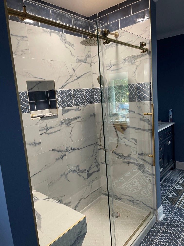 Glass walk-in shower with marble-look tile, dark blue walls, and a decorative accent band